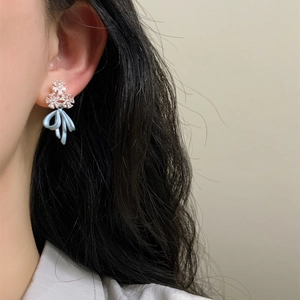 Close-up detail of elegant ice blue ribbon bow earrings with sparkling floral zircon studs.