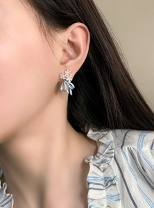 Detail showing elegant ice blue bow and crystal flower earrings on a model's ear.