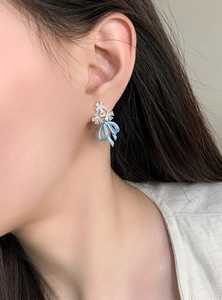 Close-up of ice blue bow earrings with sparkling crystal flower studs on a model.