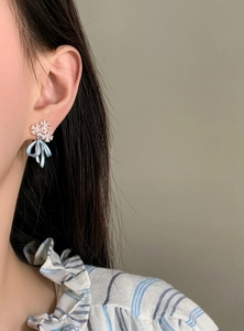 Close-up of elegant ice blue ribbon bow earrings with delicate floral stud design.