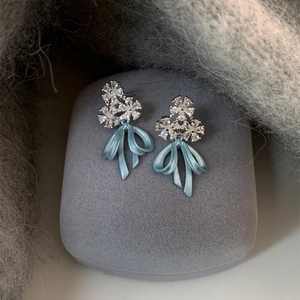 Detailed close-up of fog blue ribbon earrings with sparkling crystal flower accents.