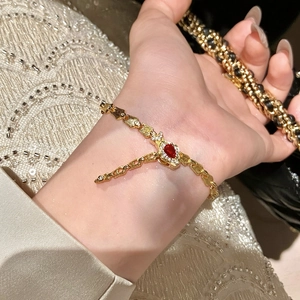 Close-up of elegant gold snake bone bracelet with a sparkling red teardrop gemstone.