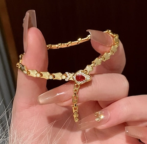 Close-up of gold snake bone bracelet featuring a vibrant red teardrop gemstone pendant