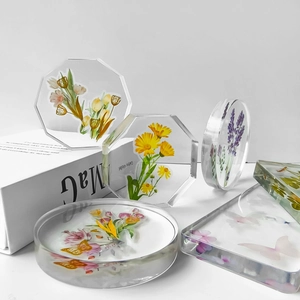 Artistic resin coasters with dried flowers and butterflies displayed on white books
