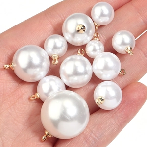 Set of white faux pearl charms with gold metal loops in various sizes shown in hand
