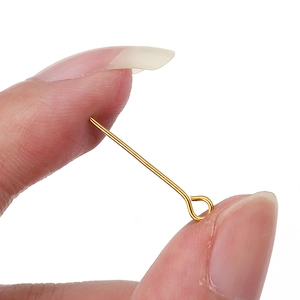 Close-up of a small 30mm golden metal eye pin for DIY jewelry making held by fingers