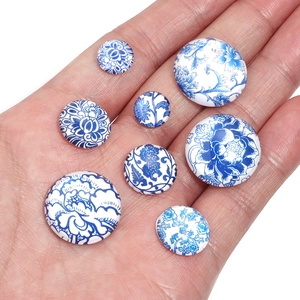 Detailed comparison of various sizes of blue and white floral glass cabochons on a hand