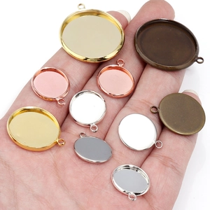 Assorted DIY round pendant bases in gold and silver, shown on palm for scale