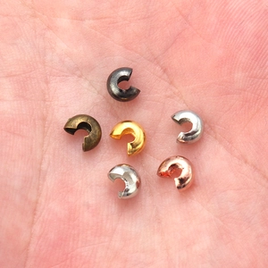 Makrofoto von 6 Metall-Quetschperlen-Abdeckungen auf einer Handfläche für DIY-Schmuck