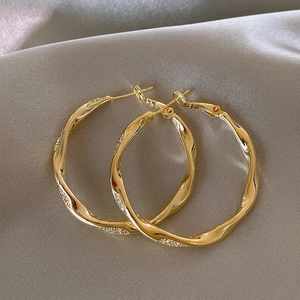 Detaillierte Nahaufnahme goldener Wellen-Ohrreifen mit Mikro-Pave-Steinen auf Satin
