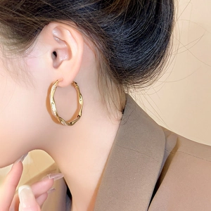 Nahaufnahme eines goldenen gewellten Creolen-Ohrrings mit Mikro-Pavé-Steinen an einem Model