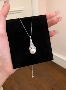 Close-up of elegant silver necklace featuring a zircon bell and white pearl pendant.