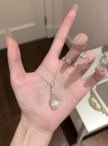 Detail view of a zirconia-paved bell-shaped pendant necklace with a large white pearl.
