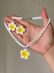 Close-up of white and yellow frangipani flower necklace and earrings set held in hand
