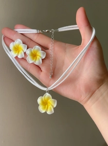 Detail view of a Hawaiian plumeria flower necklace and earring set held in hand for scale.