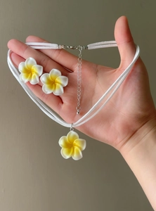 Detailed view of Hawaiian style white and yellow plumeria flower jewelry set held in hand