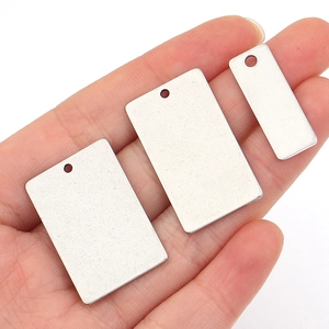 Handheld view of three rectangular stainless steel tags in different sizes for DIY jewelry
