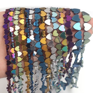 Hand holding assorted electroplated heart beads in metallic colors for DIY jewelry making