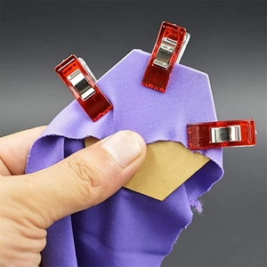 Macro detail of red sewing clips securing purple fabric and hexagonal plates on a dark base