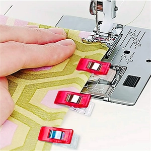 Close-up of three red sewing clips securing multi-layered fabric on a sewing machine