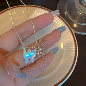 Gros plan d'un collier pendentif chat en nacre avec nœud argenté et breloque cœur.