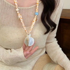 Detailed macro shot of a seashell pendant necklace featuring an orange printed ribbon