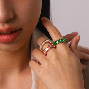 Close-up of stacked gold eternity rings with emerald green, pink, and clear zircon stones