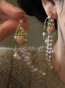 Detail view of French retro rose pearl tassel earrings worn on ear and held by hand.