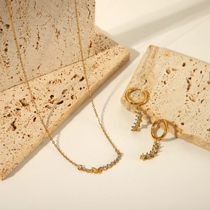Gold butterfly pendant necklace and matching crystal hoop earrings set in detail.