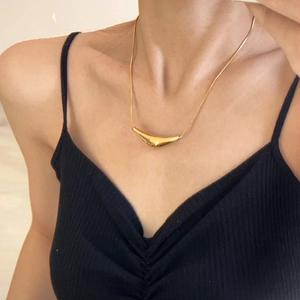 Close-up of minimalist gold curved pendant necklace on a female model wearing a black top.