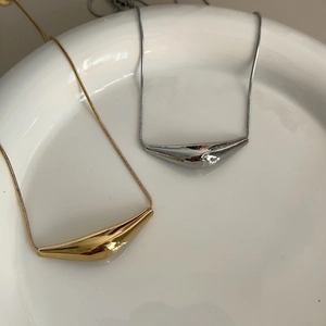 Close-up detail showing two gold and silver curved pendant necklaces on a white ceramic plate