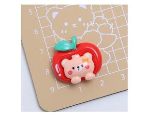 Macro di un ciondolo mela in resina rossa con orso rosa su una base graduata