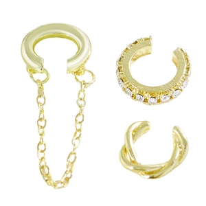 Detalle de tres ear cuffs dorados con cadena, cristales incrustados y diseño trenzado
