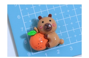 Close-up of a brown resin capybara charm holding an orange for DIY hair accessories