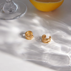 Close-up of gold stainless steel ear cuffs with zircon pavé in a sunlit lifestyle scene