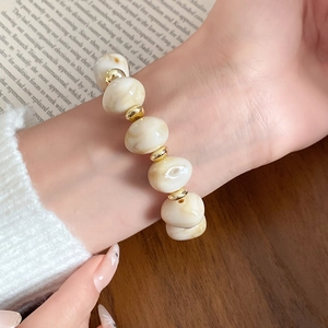 Nahaufnahme eines böhmischen Armbands mit cremefarbenen Marmorperlen und Goldakzenten