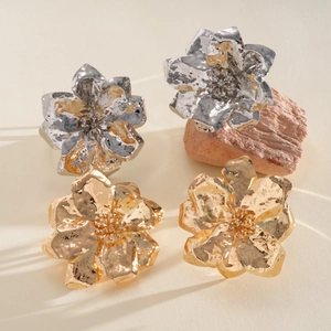 Detailed view of metallic wrinkled flower rings in gold and silver finish on stone.