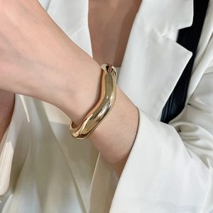 Gros plan détaillé d'un bracelet jonc en métal doré torsadé irrégulier porté au poignet.