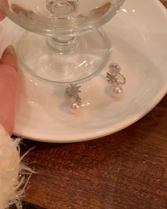 Detail view of elegant eight-pointed star pearl clip-on earrings on white saucer