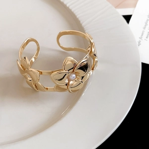 Vista dettagliata di un bracciale a polsino a fiore cavo dorato con perla centrale.