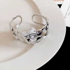 Dettaglio di un bracciale rigido aperto in metallo argentato traforato con fiore e perla