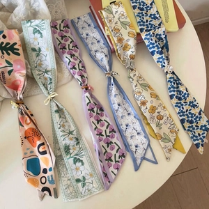 Detailed view of multiple colorful floral skinny scarves arranged on a white table