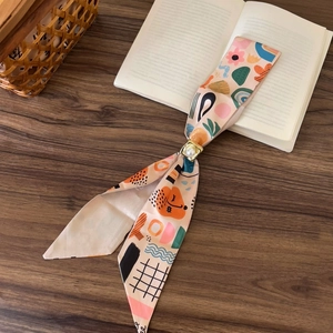 Detailed view of a colorful abstract floral skinny scarf with a pearl ring slider on a book