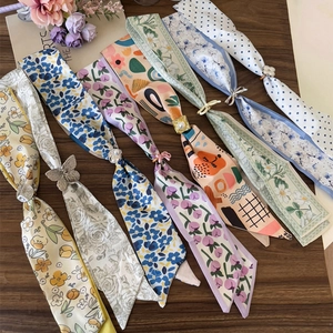 Multiple colorful floral and polka dot silk neck scarves laid out on a wooden surface