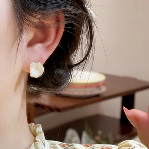 Close-up detail of elegant irregular square glass stud earrings worn on a model's ear