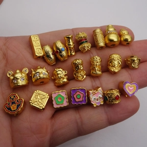 Assorted gold-plated zodiac beads and lucky pendants displayed in hand for jewelry making