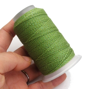 Dettaglio macro del cordoncino cerato intrecciato verde erba con paillettes su bobina