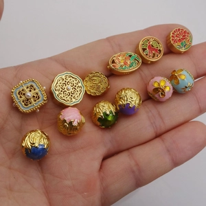 Golden enamel flower beads and butterfly charms with traditional Chinese motifs in hand
