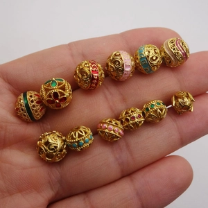 Golden hollow filigree charm beads with colorful enamel accents and traditional carvings