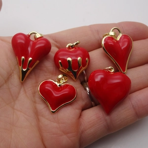 Red enamel heart pendants in drip design on hand with gold plated necklace charms